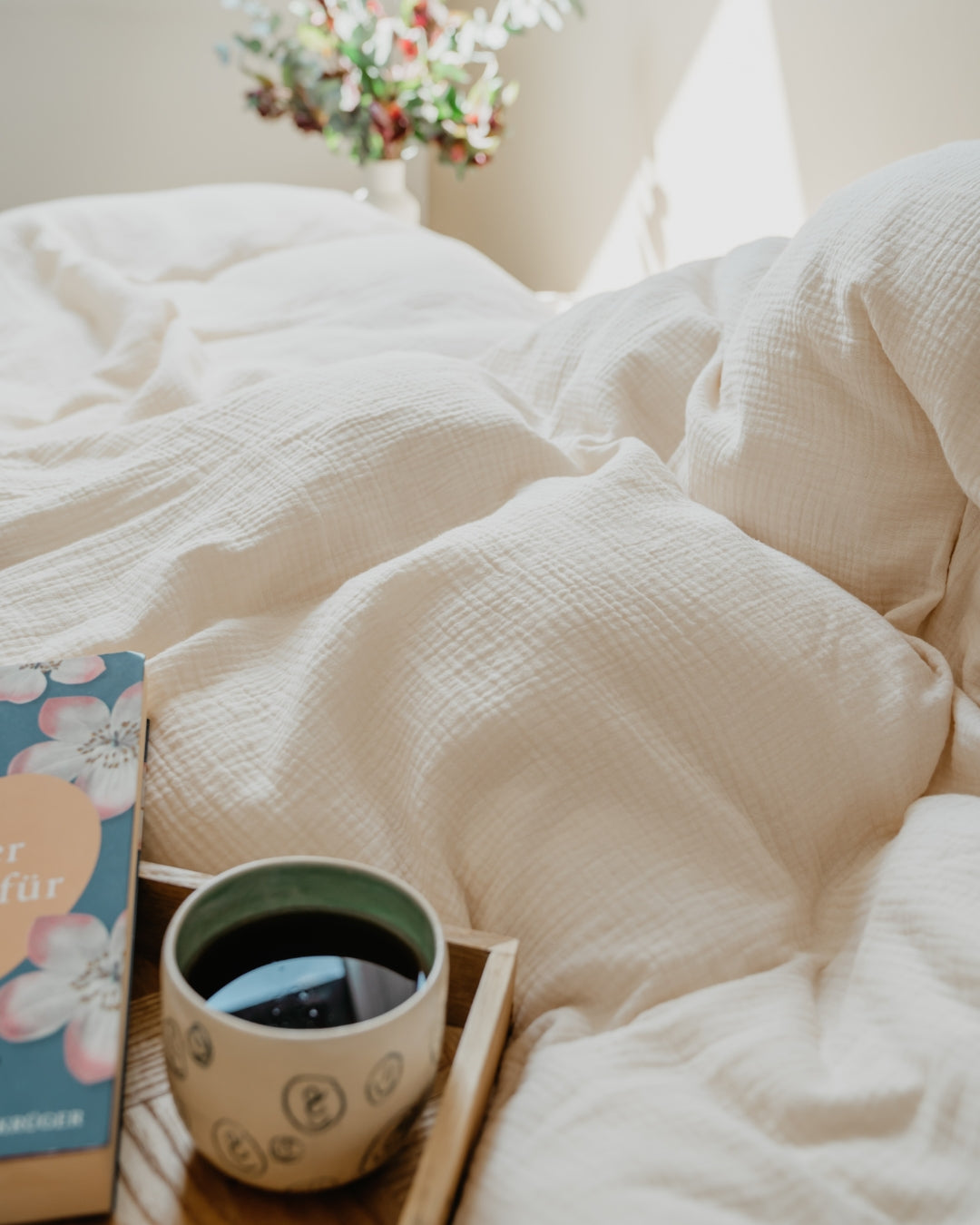 Nahaufnahme der beigefarbenen Musselin-Bettwäsche mit Buch und Tasse auf einem Tablett