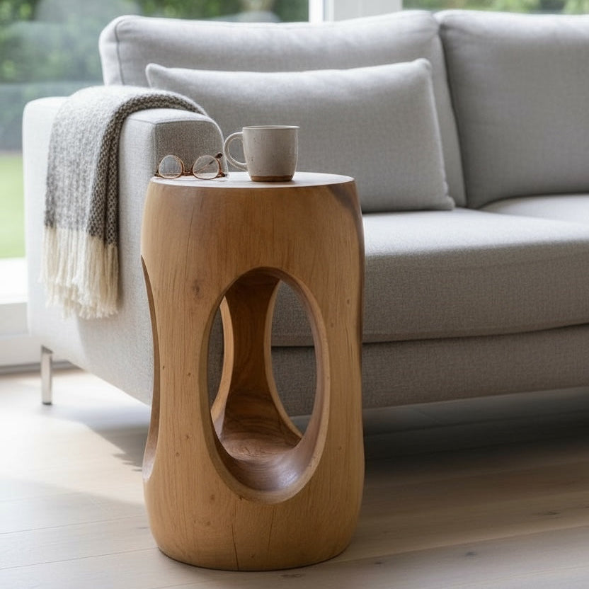 Holzbeistelltisch mit ovalem Ausschnitt neben einem hellgrauen Sofa, mit Tasse und Brille auf der Ablage.