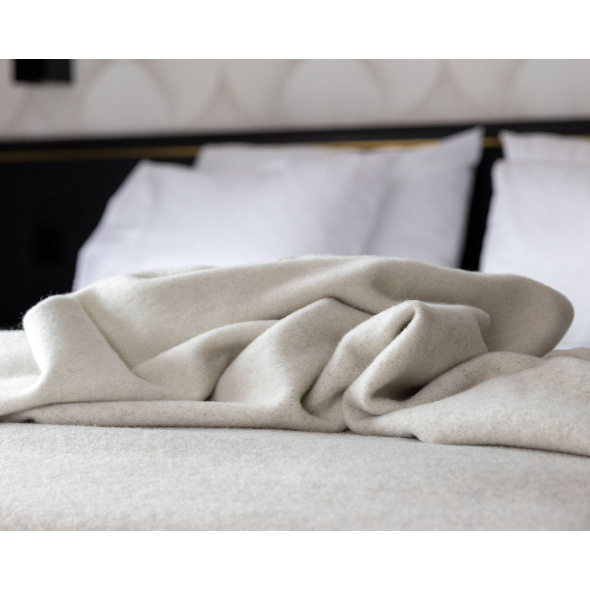 Beige-weiße Decke auf einem Bett mit weißen Kissen.
