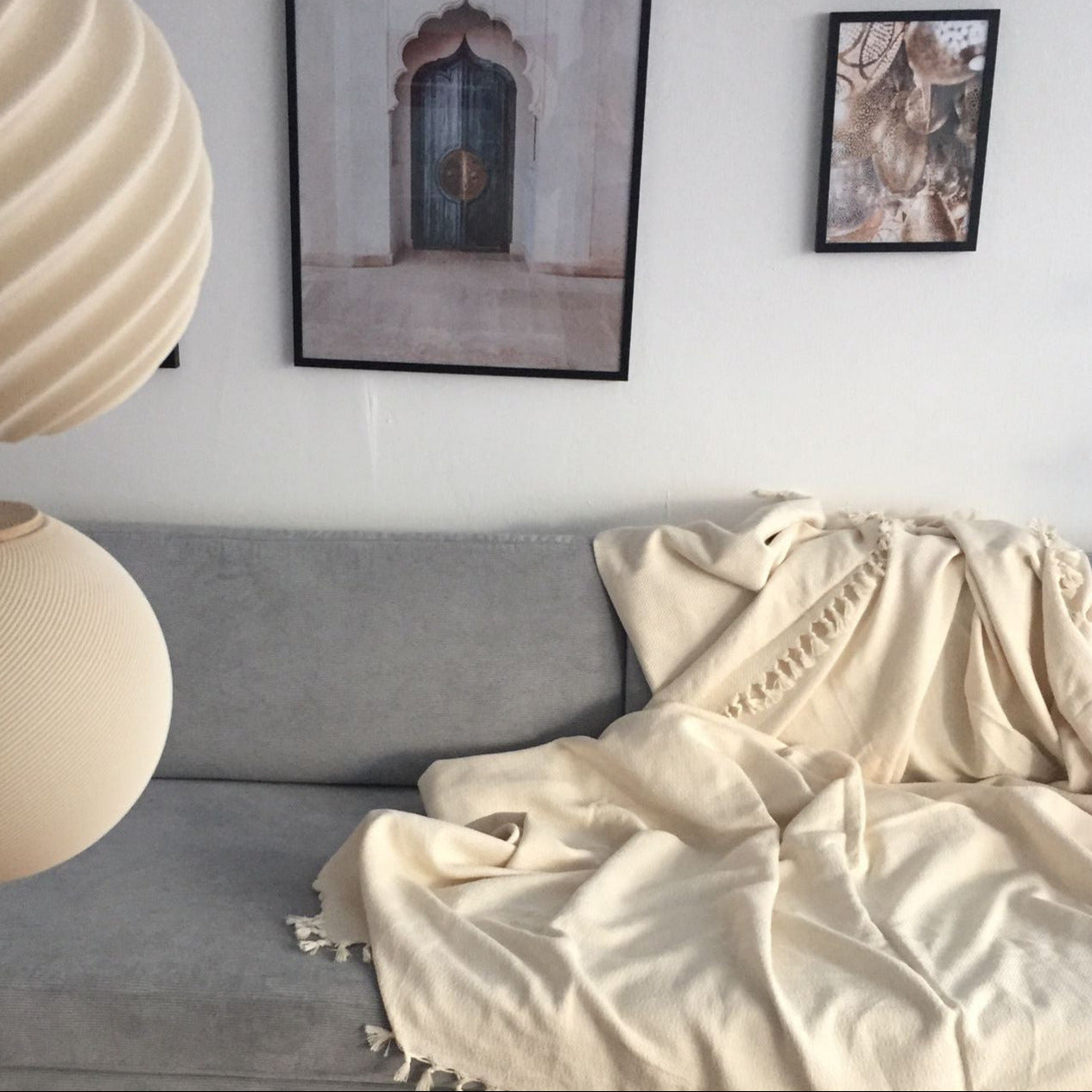 Weiche handgefertigte Bio-Baumwoll-Decke in Naturfarbe auf grauem Sofa, gemütlich arrangiert mit Wandbildern im Hintergrund